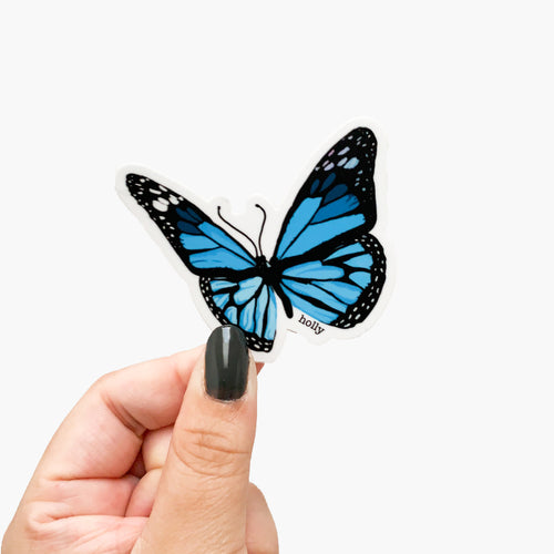 A sticker featuring an original illustration of a blue butterfly outlined in black.