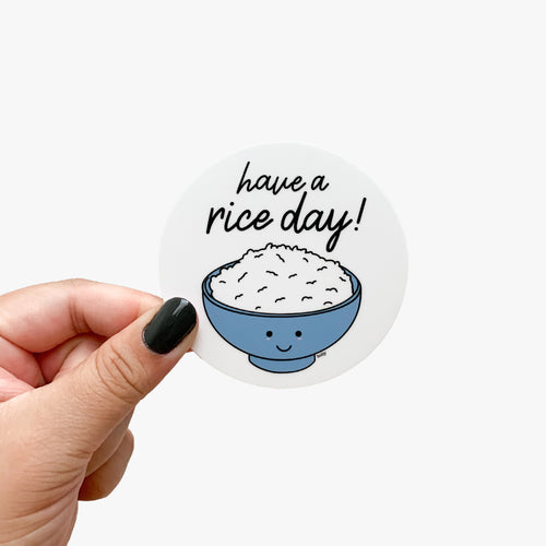 A circle sticker featuring a bowl of rice with a happy face on it and text that reads, Have a rice day!