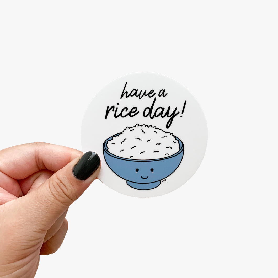 A circle sticker featuring a bowl of rice with a happy face on it and text that reads, Have a rice day!