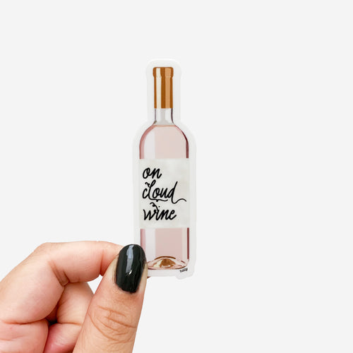 A funny sticker featuring a gold and pink wine bottle with a label that reads, On Cloud Wine.