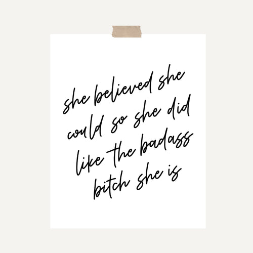 An art print featuring text that reads, “She believed she could so she did like the badass bitch she is,” written in black calligraphy hung with a piece of kraft tape on the top.